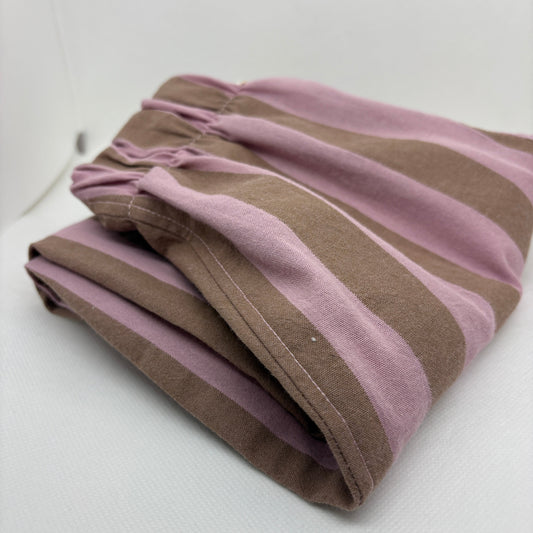 A folded pair of striped lounge pants in dusty pink and brown, displayed on a white textured surface.