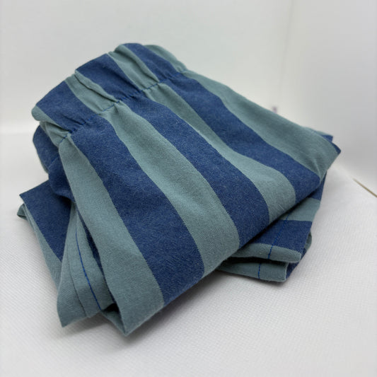 A folded pair of blue and teal striped pants or shorts with an elastic waistband, photographed on a white studio background.